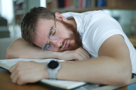 Portrait of tired overworked guy, exhausted young man in glasses college or university student is study hard in library, prepare to exam, lessonの写真素材