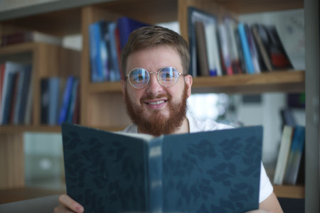 Happy young man read book in library, college or university student prepare to exam in glasses and smileの写真素材
