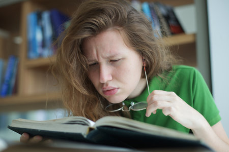 tired overworked, exhausted young woman in glasses college or university student is study hard in library, lesson, problem with eyes, myopic purblind. Vision eyes problems, myopia, blindness.の写真素材