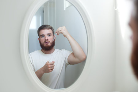young handsome bearded man apply serum oil, cosmetic product, lotion for healthy perfect fresh skin hydration, grow beard, using skincare, hydrating on white backgroundの写真素材