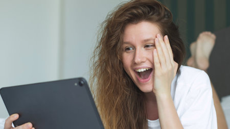 Happy young woman is using tablet computer at home in bed in bedroom, smile, have funの写真素材