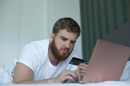 Nervous sad upset confused young man, stressed worried guy having problem with paying, buying online, payments with credit blocked bank card, looking at screen, monitor of laptop. Internet fraudの写真素材