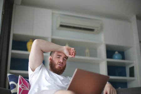Young man with air conditioner remote control using air conditioner at home, guy is cooling off...