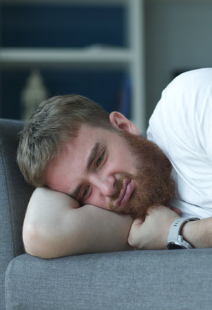 Depressed disappointed man with broken heart because of break up crying abundantly laying on sofa having psychotic moment. Male trying to stifle pain and frustration, psychological suicidal thoughtsの写真素材