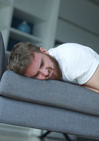 Exhausted young man fell asleep on comfortable couch in modern living room, having no energy after hard working day. Tired depressed unmotivated european guy napping on sofa at home, fatigue concept.の写真素材