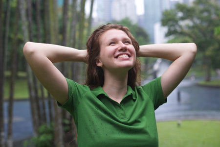 Positive young woman smiling during the rain in the park. Cheerful female enjoying the rain outdoors. Woman looking up and catching the rain drop with hands. Breath deep and relaxの写真素材