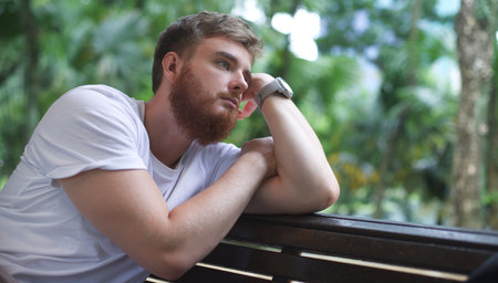 Portrait of sad upset frustrated young man, pensive thoughtful guy sit on bench in park and dreamingの写真素材