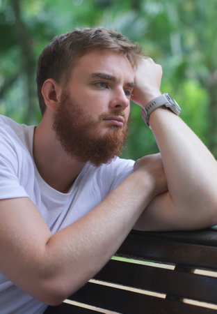 Portrait of sad upset frustrated young man, pensive thoughtful guy sit on bench in park and dreamingの写真素材