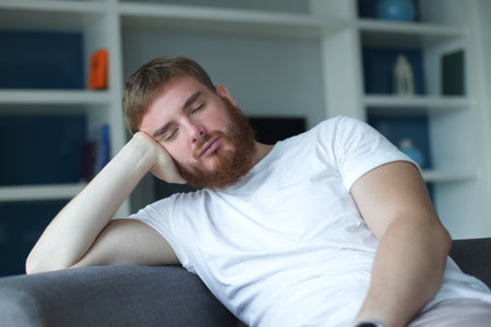 young man at home sitting on the sofa tired yawning, sleepless,bored in the living room at home interiorの写真素材