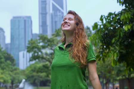 Positive young woman smiling during the rain in the park. Cheerful female enjoying the rain outdoors. Woman looking up and catching the rain drop with hands. Breath deep and relaxの写真素材