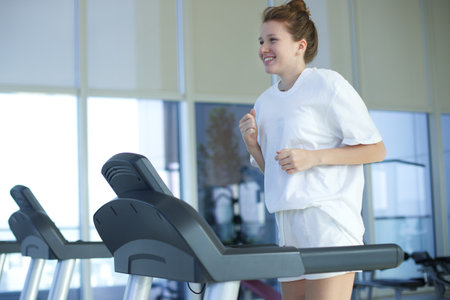 Happy young fit woman training in the gym, running jogging on treadmill, doing cardio exercise and...