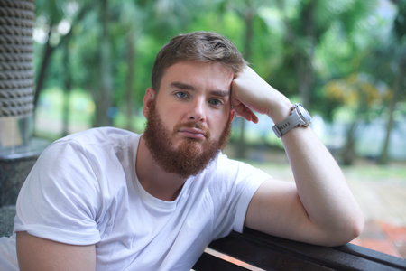 Portrait of sad upset frustrated young man, pensive thoughtful guy sit on bench in park and dreamingの写真素材