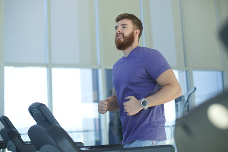 Happy young fit man training in the gym, running jogging on treadmill, doing cardio exercise and smile. Healthy lifestyle, sport, fitness conceptの写真素材