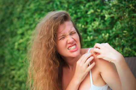 Irritated young suffering woman scratching her itching arm from a mosquito bite at the park at summer sunny day, itchy insect biteの写真素材