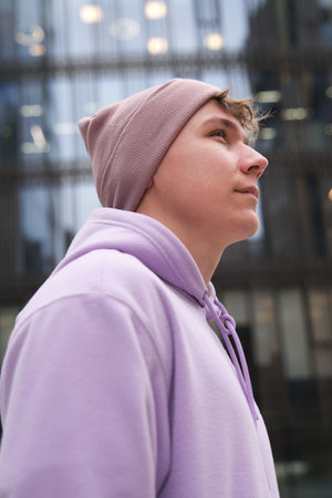 Portrait of young happy man or teenager in hoodie and hat looking at camera outdoors