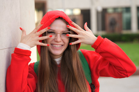 beautiful young college or university student, happy girl outdoors at campus in glasses with braces. Portrait of teen, female teenager in red hoodの写真素材