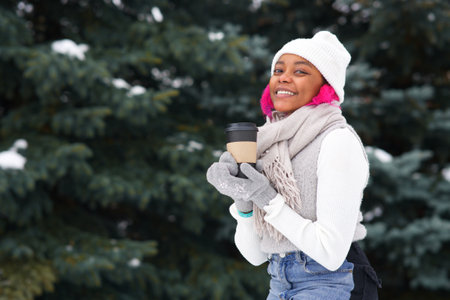 Portrait of happy Afro American young woman at winter snowy day in snow park smile, drink coffeeの写真素材