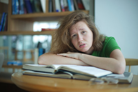 Portrait of tired overworked girl, exhausted young woman in glasses college or university student is study hard in library, prepare to exam, lessonの写真素材