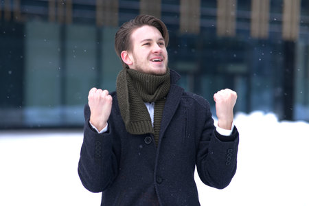 Young happy successful man celebrating triumph, victory at winter snowy dayの写真素材