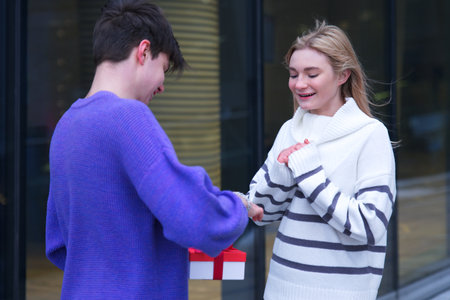 beautiful happy young couple, teenager girl and teen boy. Handsome guy boyfriend is presenting his girlfriend and giving her box with present Christmas gift at Saint Valentines Day. Love, happinessの写真素材