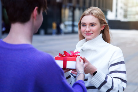 beautiful happy young couple, teenager girl and teen boy. Handsome guy boyfriend is presenting his girlfriend and giving her box with present Christmas gift at Saint Valentines Day. Love, happinessの写真素材
