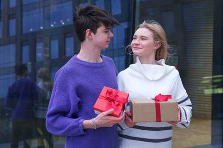 beautiful happy young couple, teenager girl and teen boy. Handsome guy boyfriend is presenting his girlfriend and giving her box with present Christmas gift at Saint Valentines Day. Love, happinessの写真素材