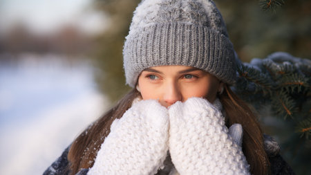 Portrait of beautiful girl young frozen pretty woman standing walking in winter snowy park at cold snow frosty day in hat, scarf, in gloves looking at cameraの写真素材