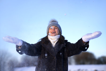Portrait of beautiful girl young frozen pretty woman standing walking in winter snowy park at cold snow frosty day in hat, scarf, in gloves looking at cameraの写真素材