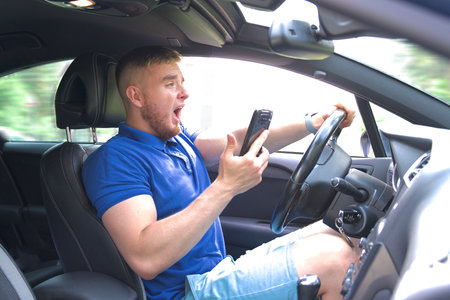 Scared careless man driver drive car and use mobile cell phone. Dangerous situation, crash the carの写真素材