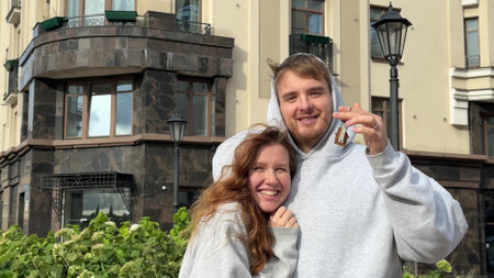 young married couple with keys to a new apartment against the background of the houseの写真素材