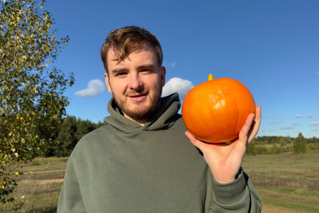 Happy young man farmer hold ripe orange pumpkin in hand and smile on natural backgroundの写真素材