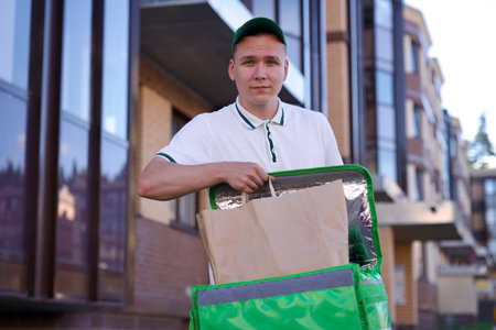Happy young man courier in green uniform with big thermo bag or backpack deliver food from...
