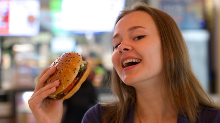 Portrait of young happy woman or beautiful teenager girl eating fast junk food, tasty burger and...