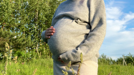 Close up of unrecognised pregnant woman stroking, touching her belly at nature at summer dayの写真素材