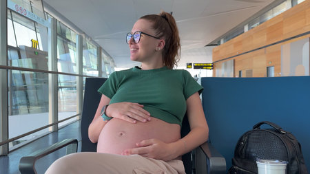 happy pregnant woman traveling alone, waiting for plane at airport, second or third trimester