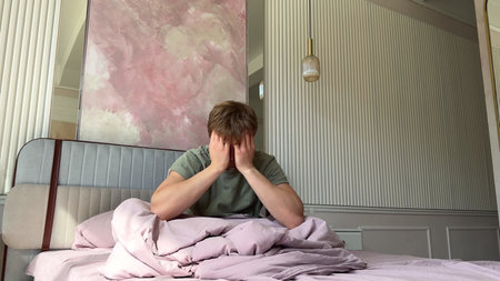 Sad frustrated depressed young man sitting in bed in the morning