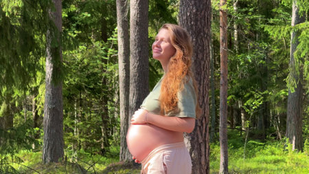 young pregnant woman walking in summer pine forest and stroking her bellyの写真素材