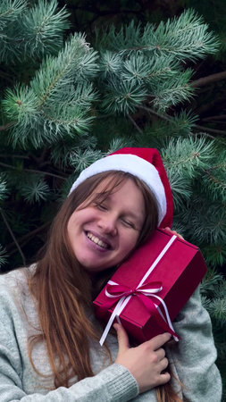 Happy young woman holding present box in hands on Christmas tree background