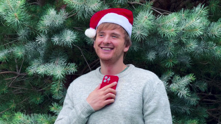 Young happy overjoyed man in Christmas hat looking at his cell mobile phone and having fun