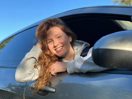 young wooman or teenage girl sit behind the wheel of her own car, positive and happy