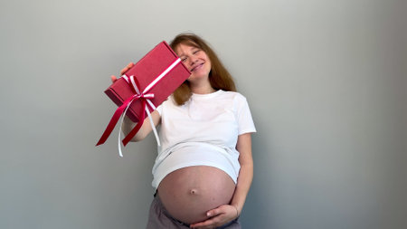 young happy pregnant woman holding Christmas present box in handsの写真素材