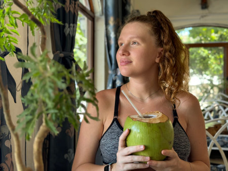 beautiful young woman drinking fresh coconut in cafe in summer in tropical countryの写真素材