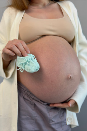 beautiful pregnant woman holding her future babys booties with her big belly in the backgroundの写真素材