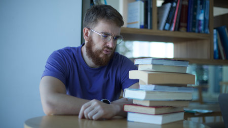 sad man student in glasses, sitting with books in library. concept education, university, college,...