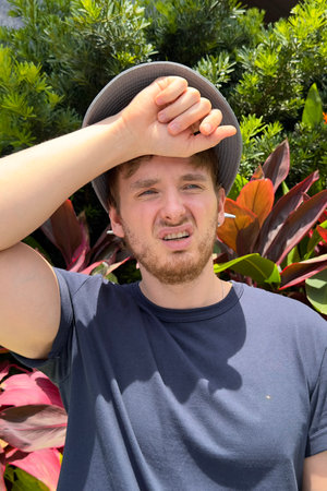 Young man is suffering from heat, having sunstroke at summer day