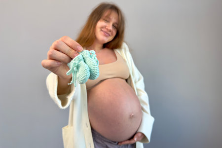 beautiful pregnant woman holding her future babys booties with her big belly in the backgroundの写真素材