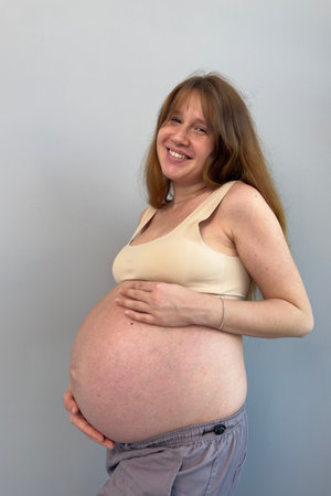 Happy pregnant young woman on gray background