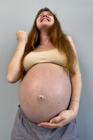 Happy pregnant young woman on gray backgroundの写真素材