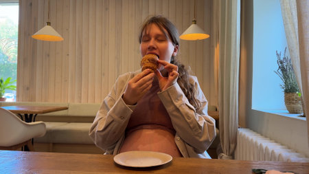 Young pregnant hungry woman eating croissant in cafeの写真素材