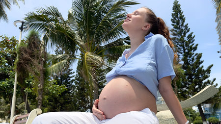 A Beautiful Pregnant Woman Enjoying a Relaxing Day Under Palm Trees at the Beach